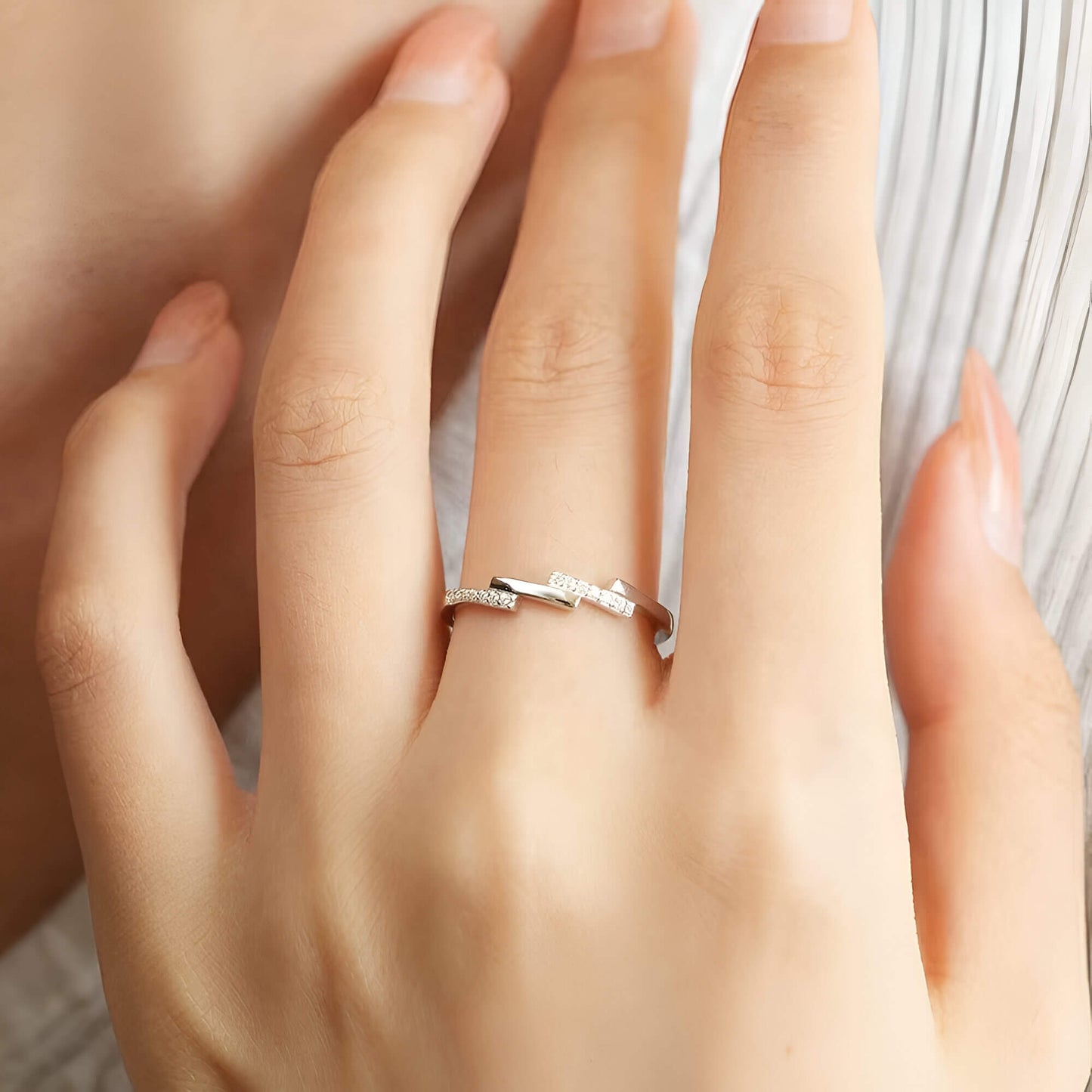 Alliance asymétrique en acier inoxydable et or blanc sertie d'oxydes de zirconium portée au doigt d'une femme vue du dessus.