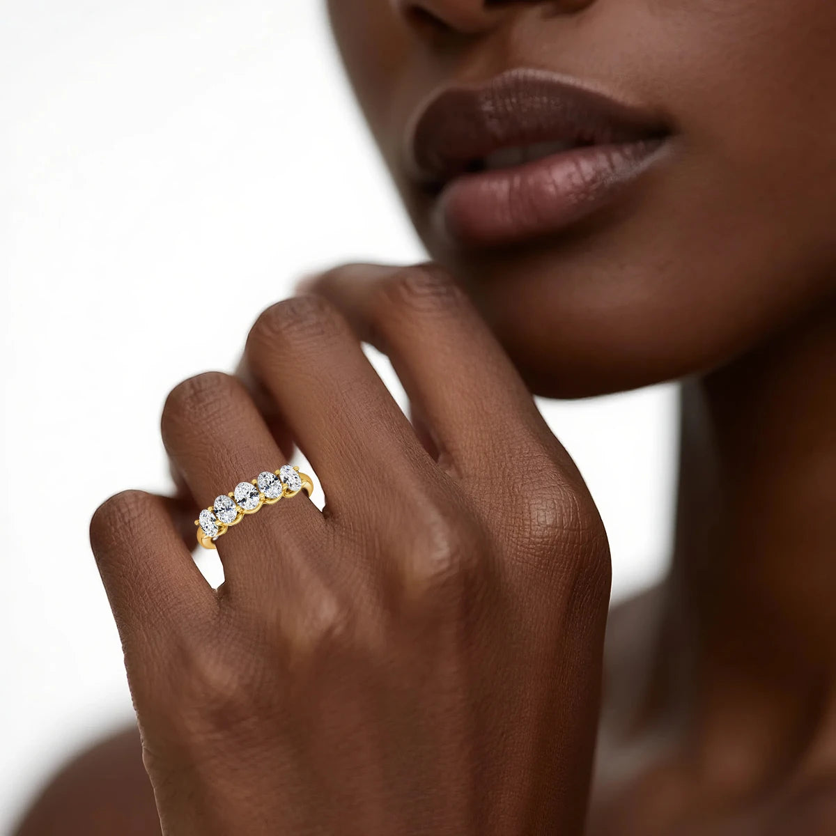 Alliance cinq pierres en or jaune et diamants synthétiques portée au doigt d'une femme.