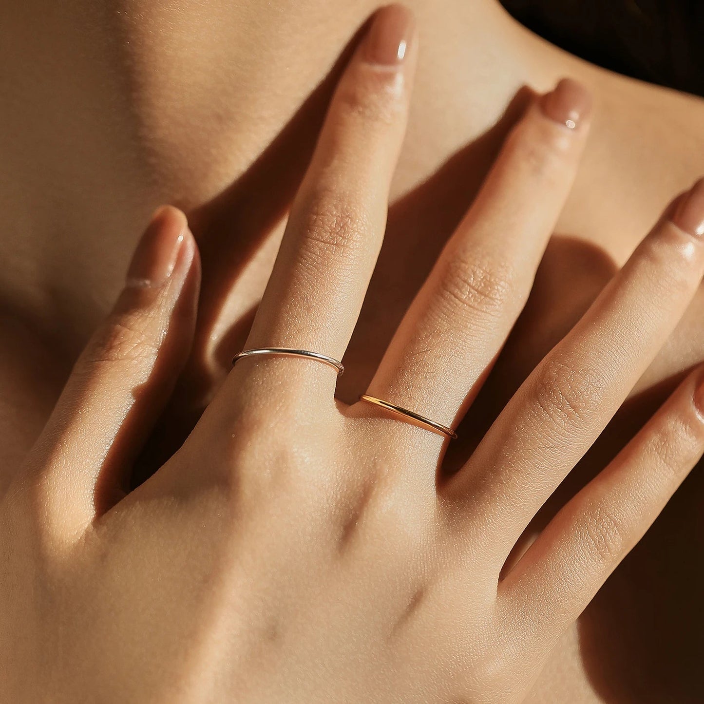 Main de femme portant aux doigts l'alliance fine et simple variantes or jaune et or blanc.