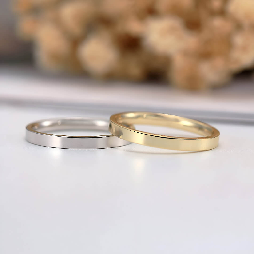 Alliances ruban épurées en or jaune et or blanc posées.
