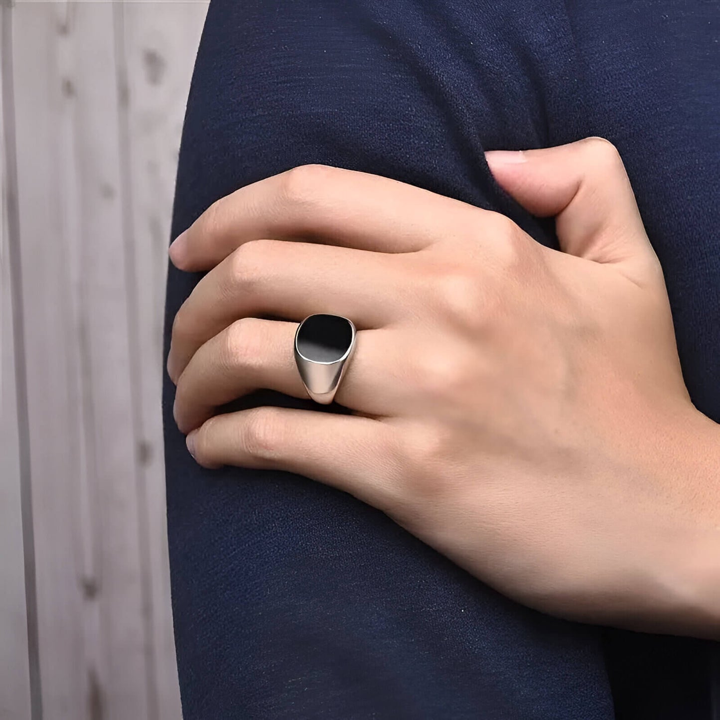 Bague chevalière en acier et or blanc sertie d'onyx portée au doigt d'un homme.