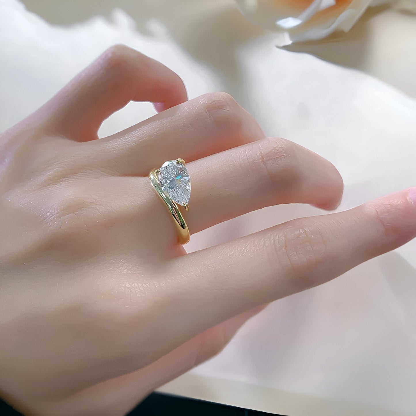 Main de femme portant la bague de fiançailles en or 18K avec saphir goutte, élégance et raffinement pour un engagement précieux.