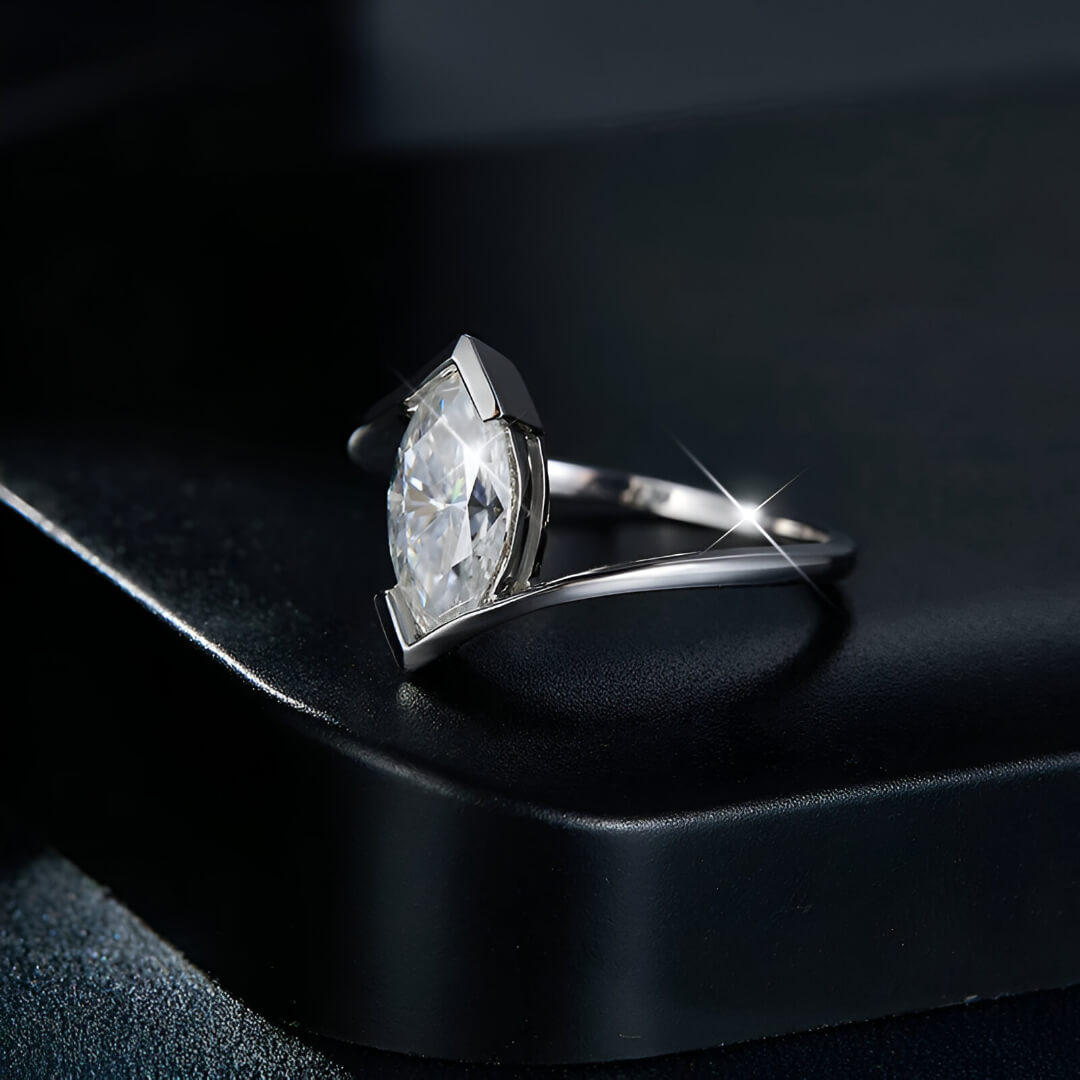 Bague moissanite marquise solitaire en argent à plat vue de côté sur une surface noire.