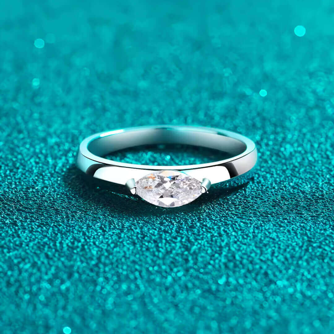 Bague solitaire dune de diamant à plat vue de face sur fond bleu cyan.