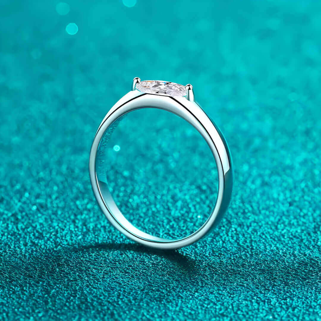 Bague solitaire dune de diamant vue latérale sur du granite bleu cyan.
