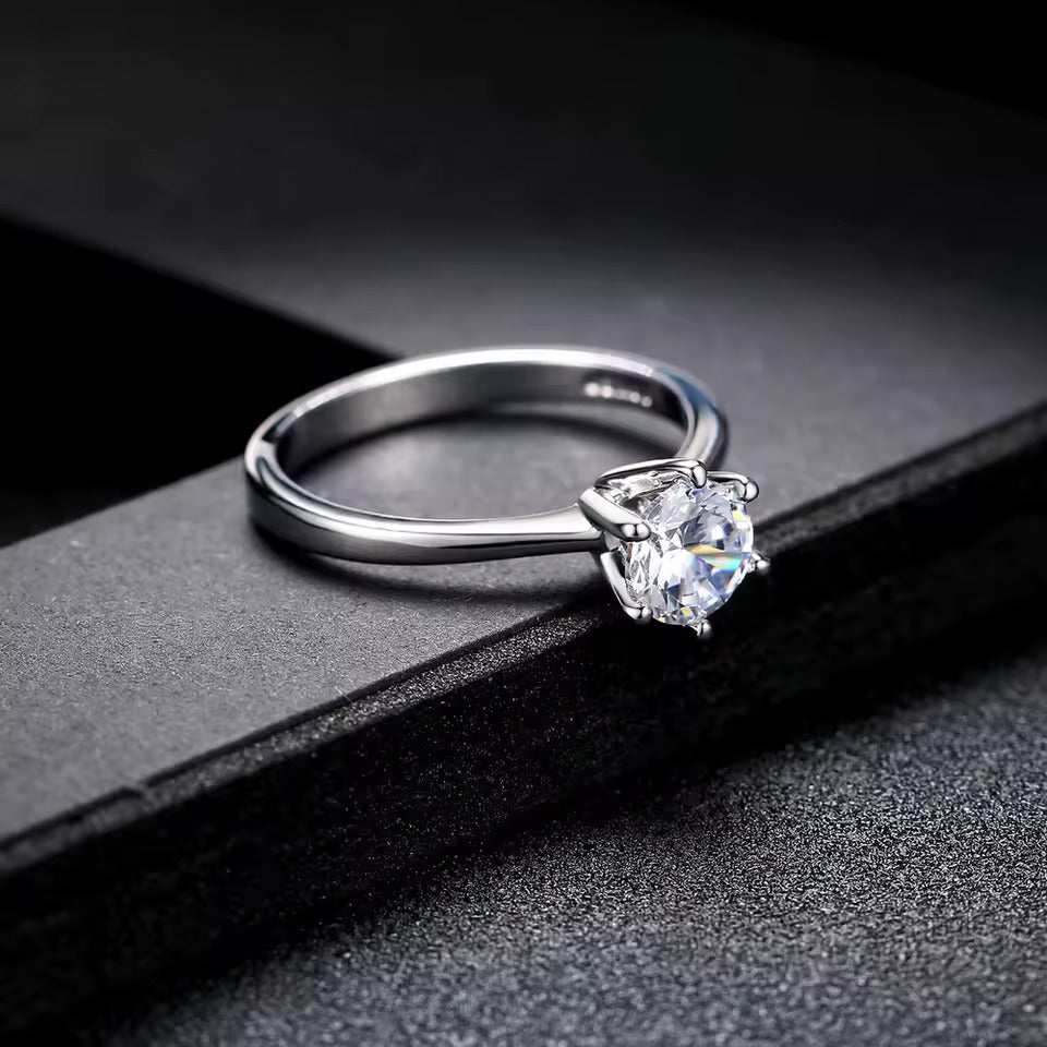 Bague solitaire six griffes en argent à plat vue de côté sur un rebord noir.