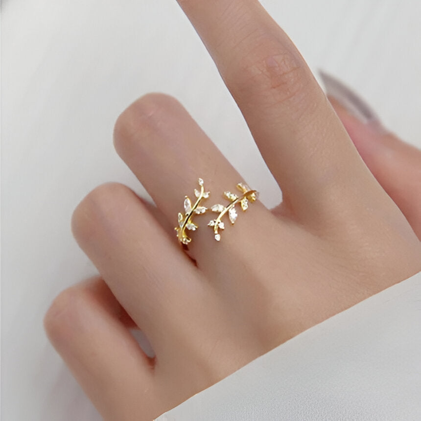 Bague fantaisie ouverte en or jaune et oxyde de zirconium portée au doigt d'une femme vue du dessus.