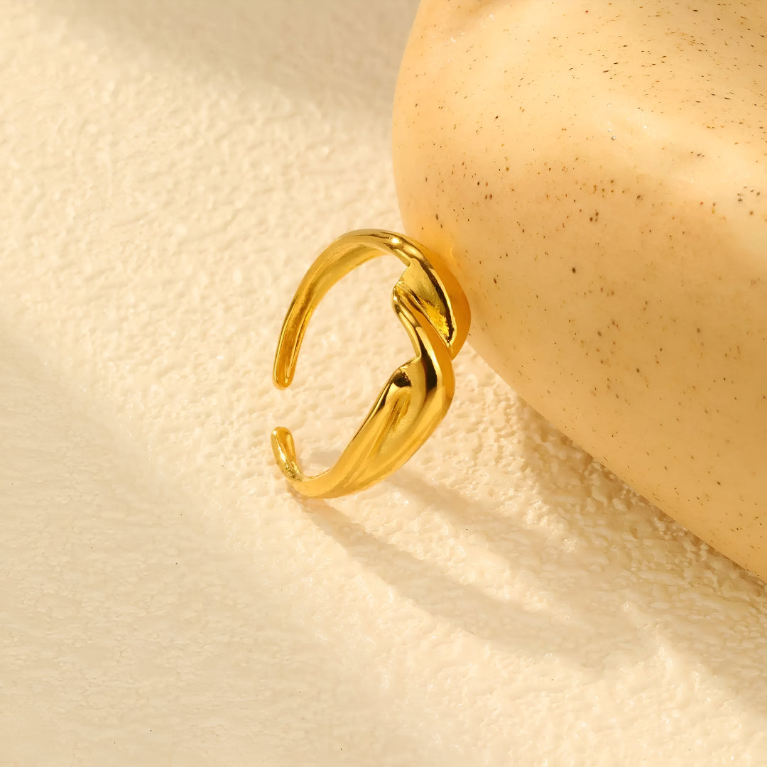 Bague ouverte en or 18K torsion lumineuse, posée délicatement sur une pierre, offrant un contraste chic et naturel. Un bijou parfait pour ajouter une touche d’élégance à chaque tenue.