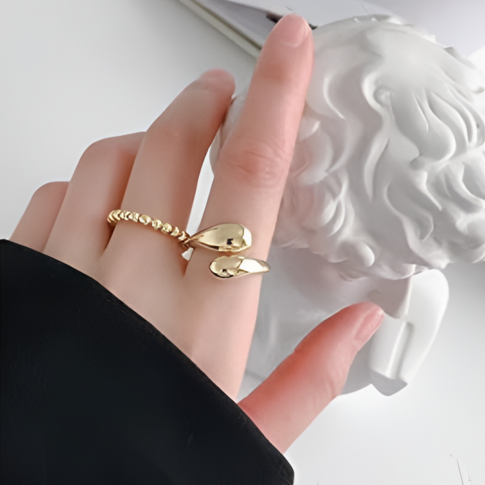 Bague ouverte en or Goutte d'eau 14K sur la main d'une femme, alliant simplicité et sophistication. Design luxueux, idéale pour rehausser chaque tenue.