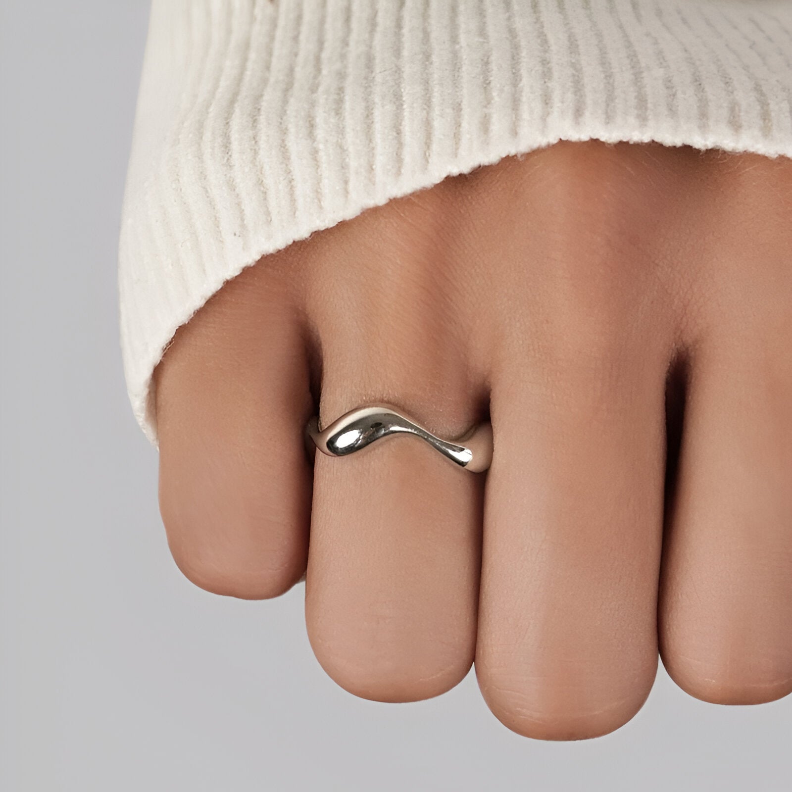 Bague ouverte ondulée en or blanc portée au doigt d'une femme vue rapprochée.