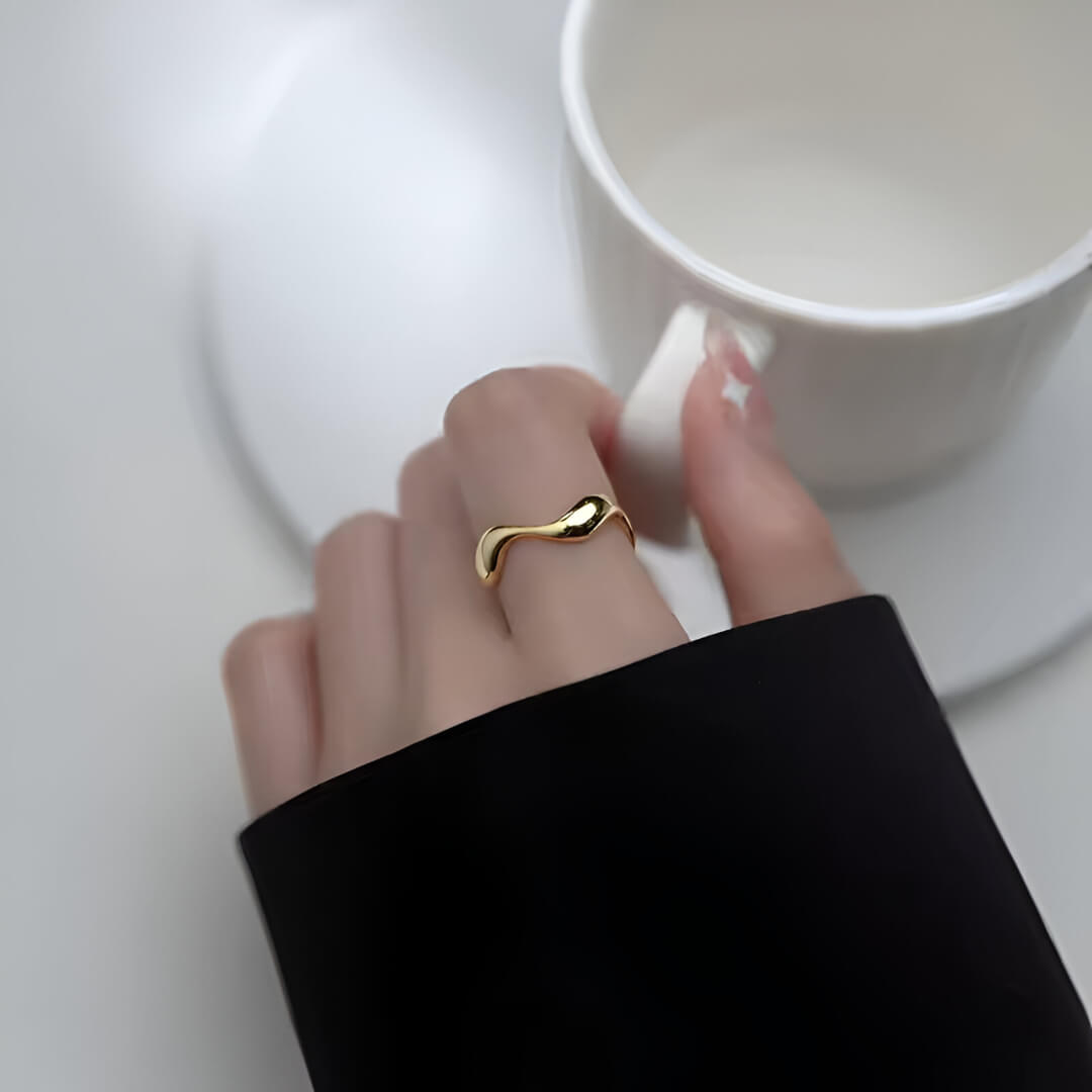 Bague ouverte ondulée en or jaune portée au doigt d'une femme vue du dessus.