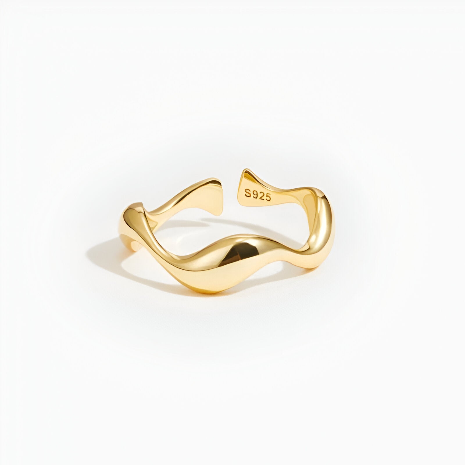 Bague ouverte ondulée en or jaune sur fond blanc.