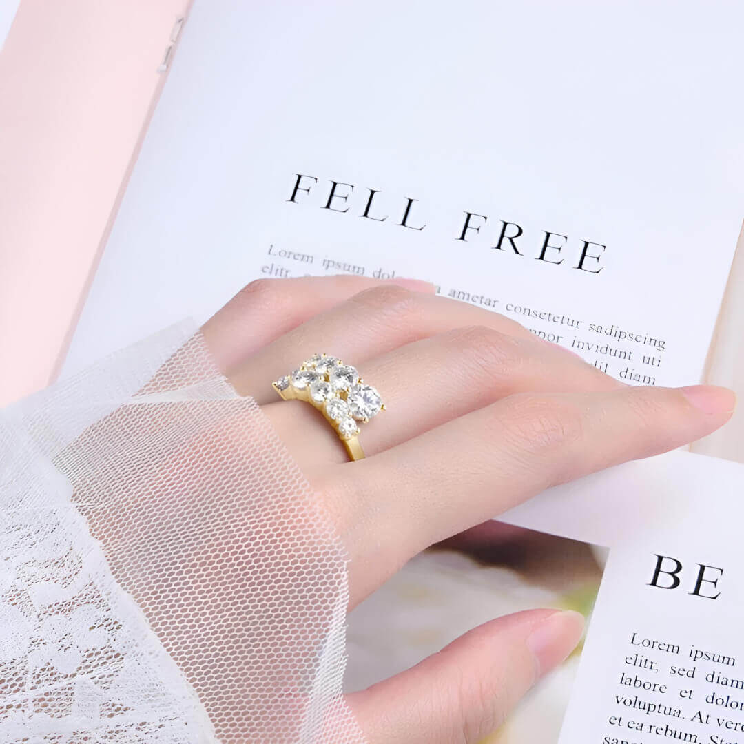 Bague ouverte en or jaune et diamants synthétiques portée au doigt d'une femme vue de loin.