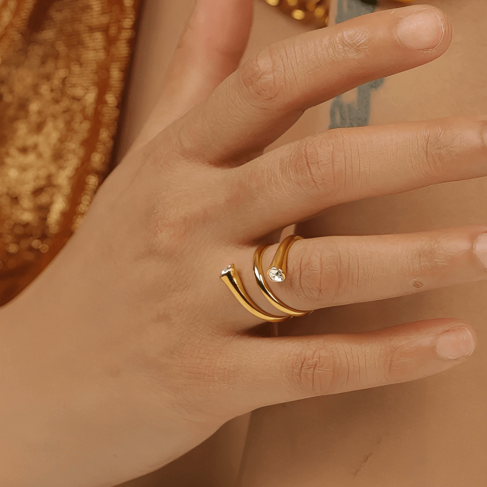 Bague fantaisie ouverte tourbillon en acier inoxydable et or jaune sertie de cristaux portée au doigt d'une femme vue rapprochée.