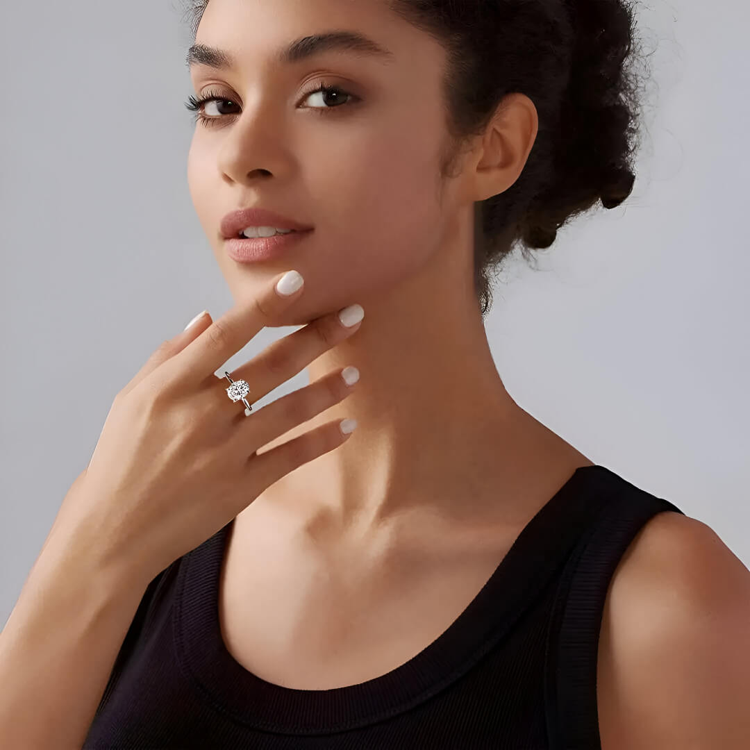 Bague solitaire en or blanc et diamant synthétique portée au doigt d'une femme brune.