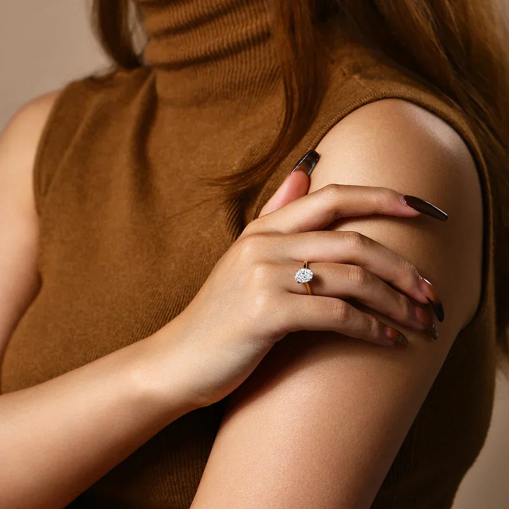 Bague solitaire en or jaune et diamant synthétique portée au doigt d'une femme vue de loin.