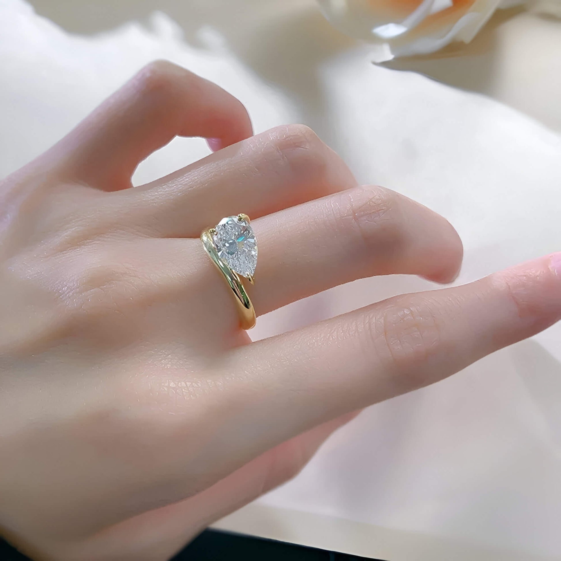 Bague solitaire courbée en or jaune et diamant synthétique portée au doigt d'une femme.