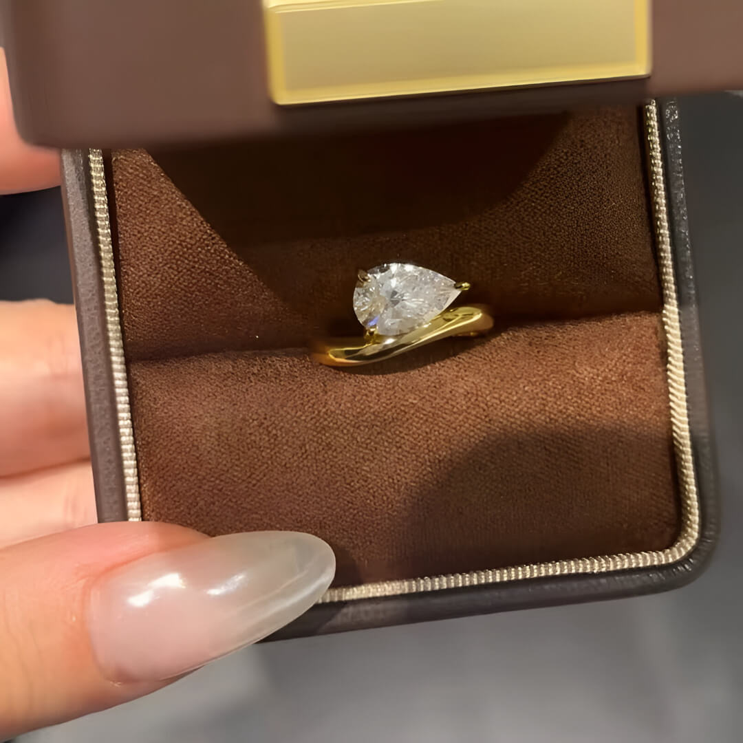 Bague solitaire courbée en or jaune et diamant synthétique dans son écrin.