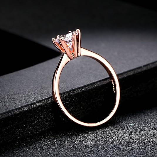 Bague solitaire en or rosé et oxyde de zirconium posée sur un rebord noir.