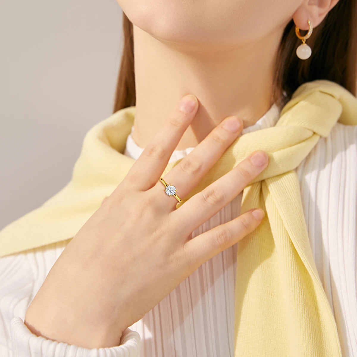 Bague solitaire quatre griffes en or jaune et diamant synthétique portée au doigt d'une femme.