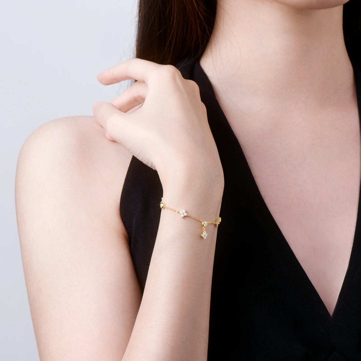 Bracelet à breloques en or jaune et diamants synthétiques porté au poignet d'une femme vue de loin.