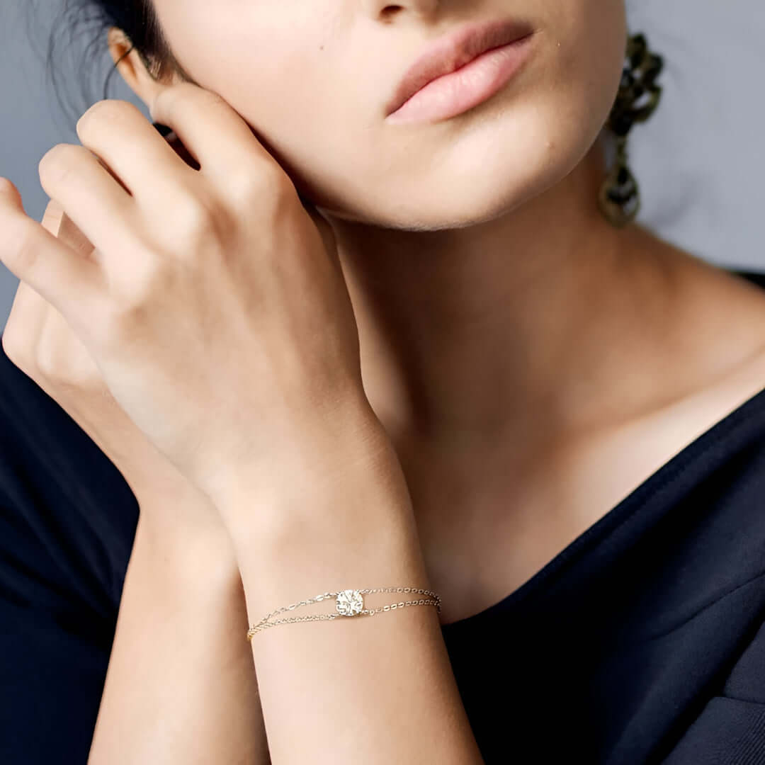 Bracelet chaîne double argentée en argent 925 plaqué or blanc et moissanite solitaire porté au poignet d'une femme vue de proche.