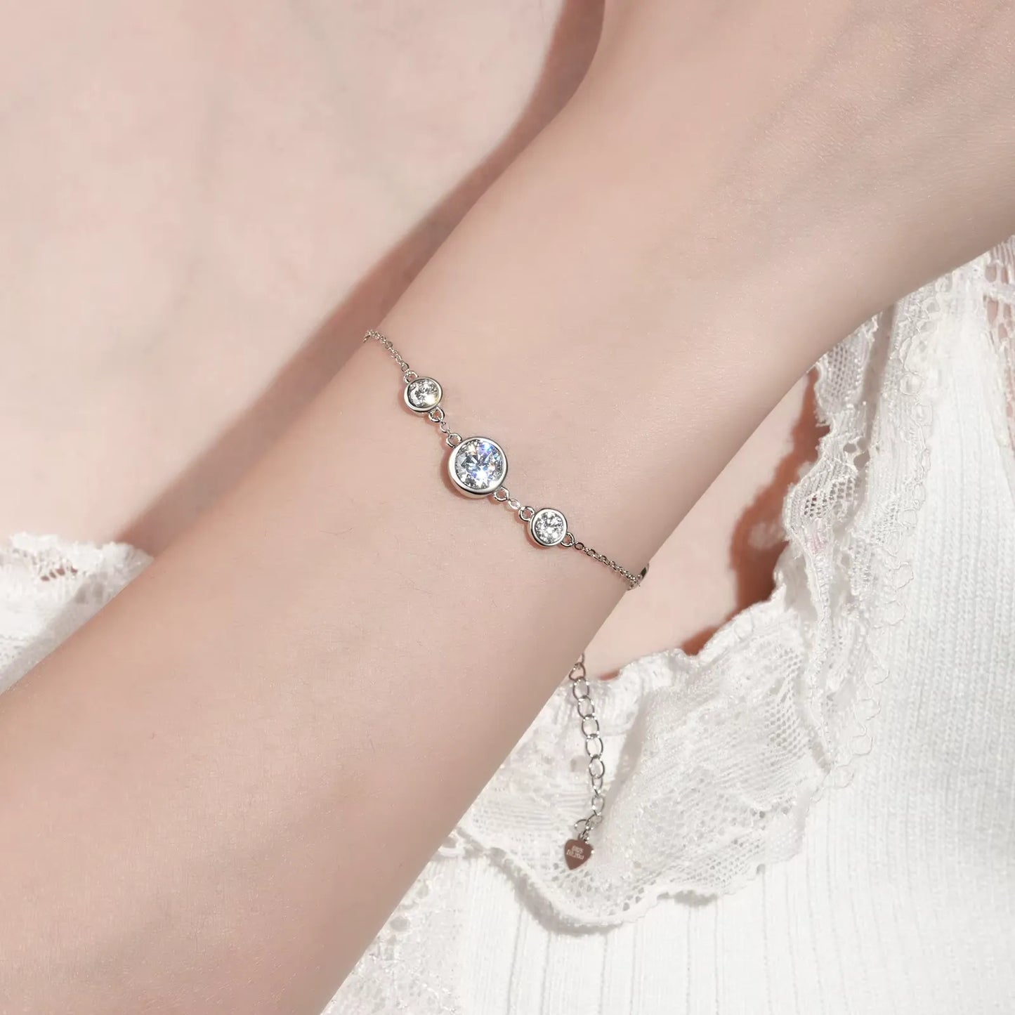 Chaîne cinq pierre en or blanc et diamants synthétiques portée au poignet d 'une femme.