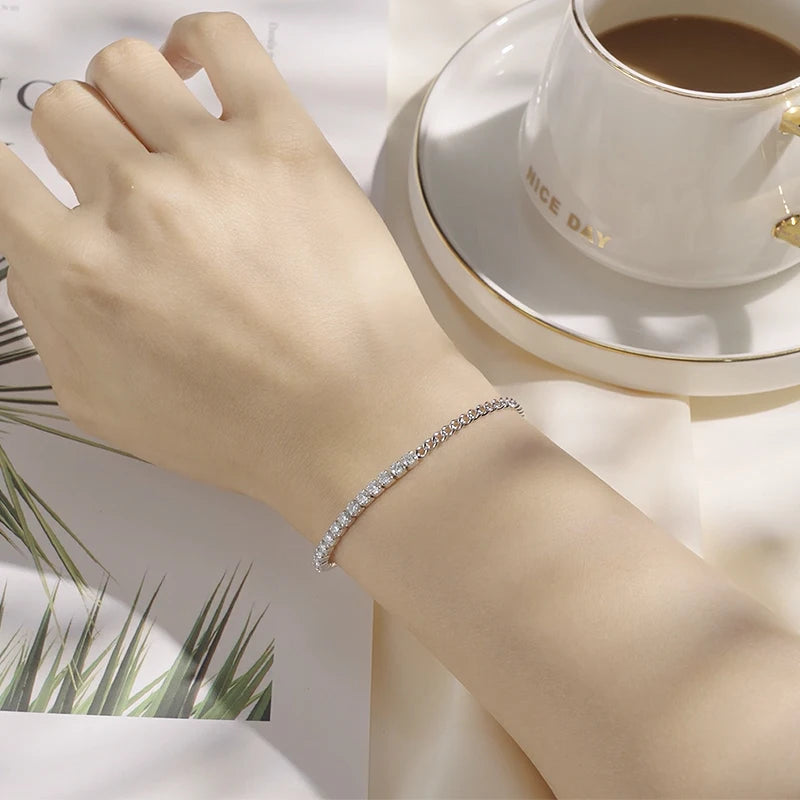 Chaîne gourmette en or blanc et diamants synthétiques portée au poignet d'une femme.