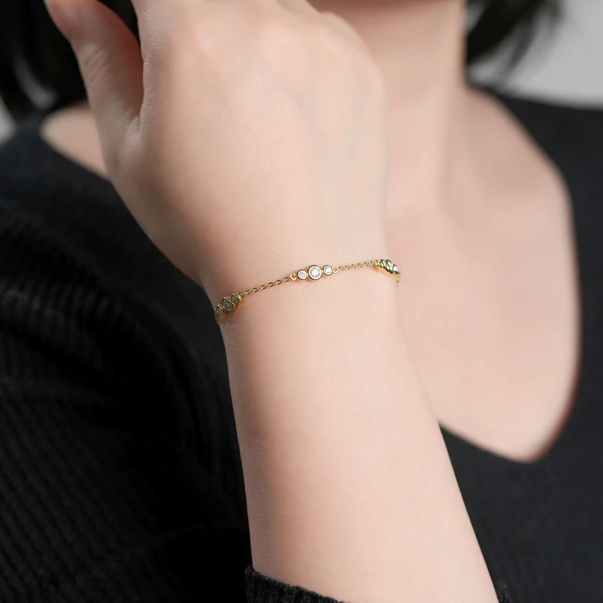 Chaîne triple pierres en or jaune et diamants synthétiques portée au poignet d'une femme vue de face.