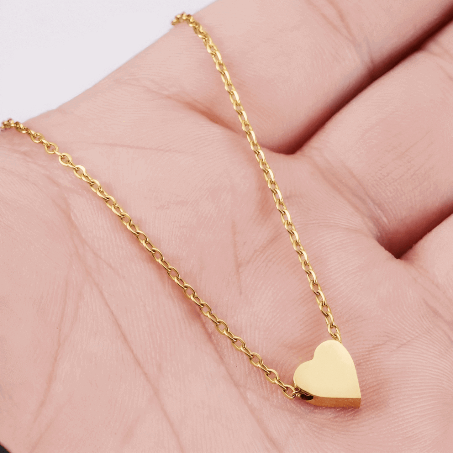 Collier fantaisie cœur en or jaune montré par une main de femme.