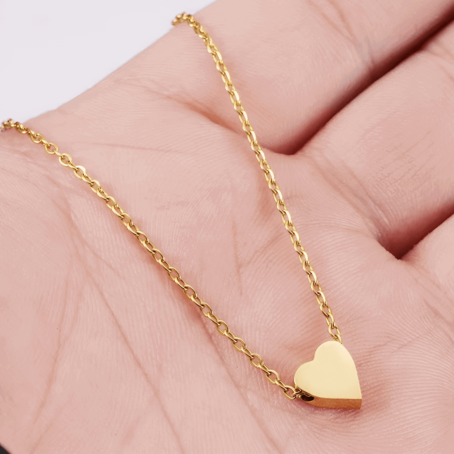 Collier fantaisie cœur en or jaune montré par une main de femme.