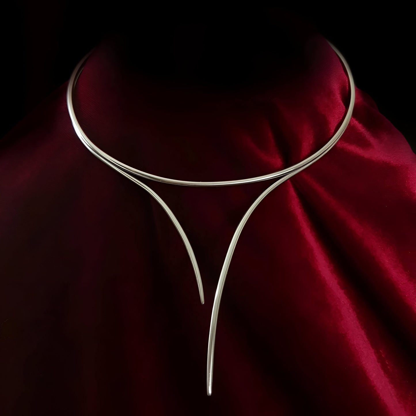 Collier Torque Courbes Enlacées en alliage de zinc plaqué or blanc, mis en valeur sur fond noir et rouge