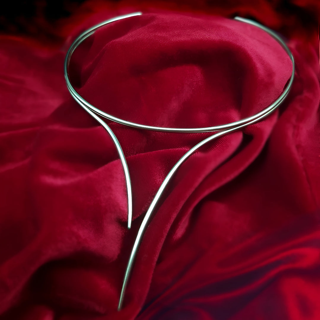 Collier élégant Torque Courbes Enlacées posé sur tissu rouge, finition or blanc