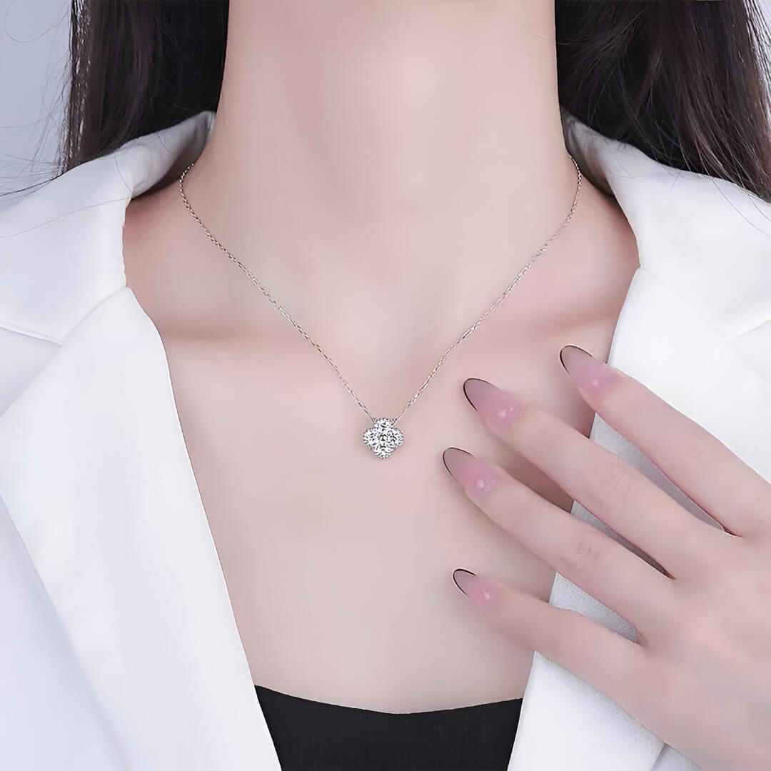 Collier trèfle à quatre feuilles en or blanc et diamants synthétiques porté au cou d'une femme vue de face.