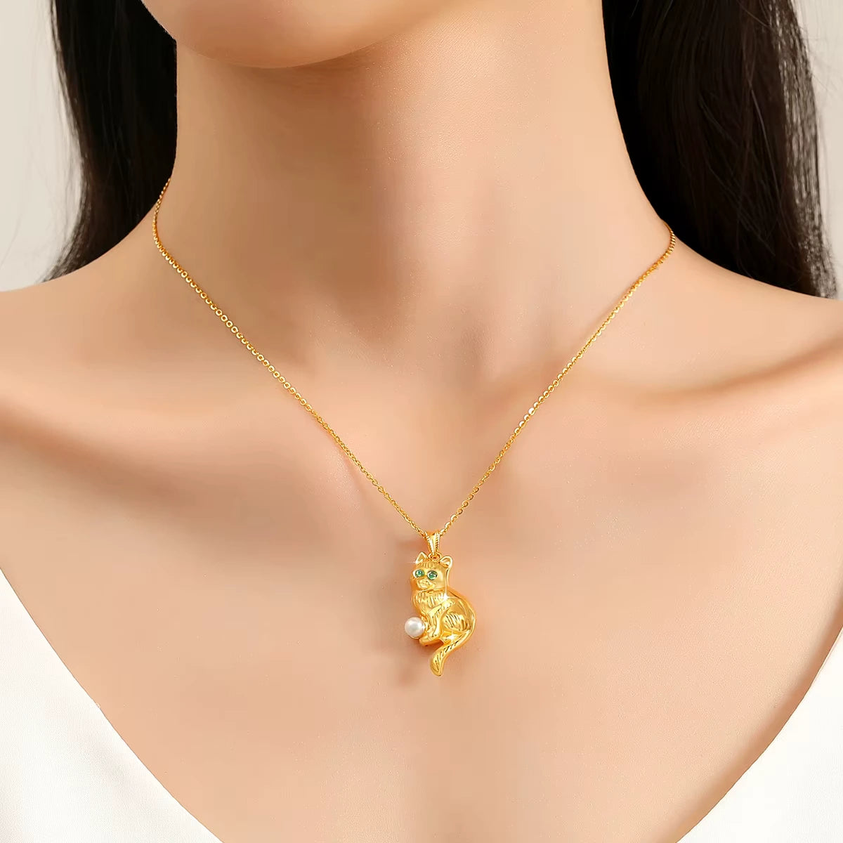 Pendentif chat en or jaune et perle ronde porté au cou d'une femme.