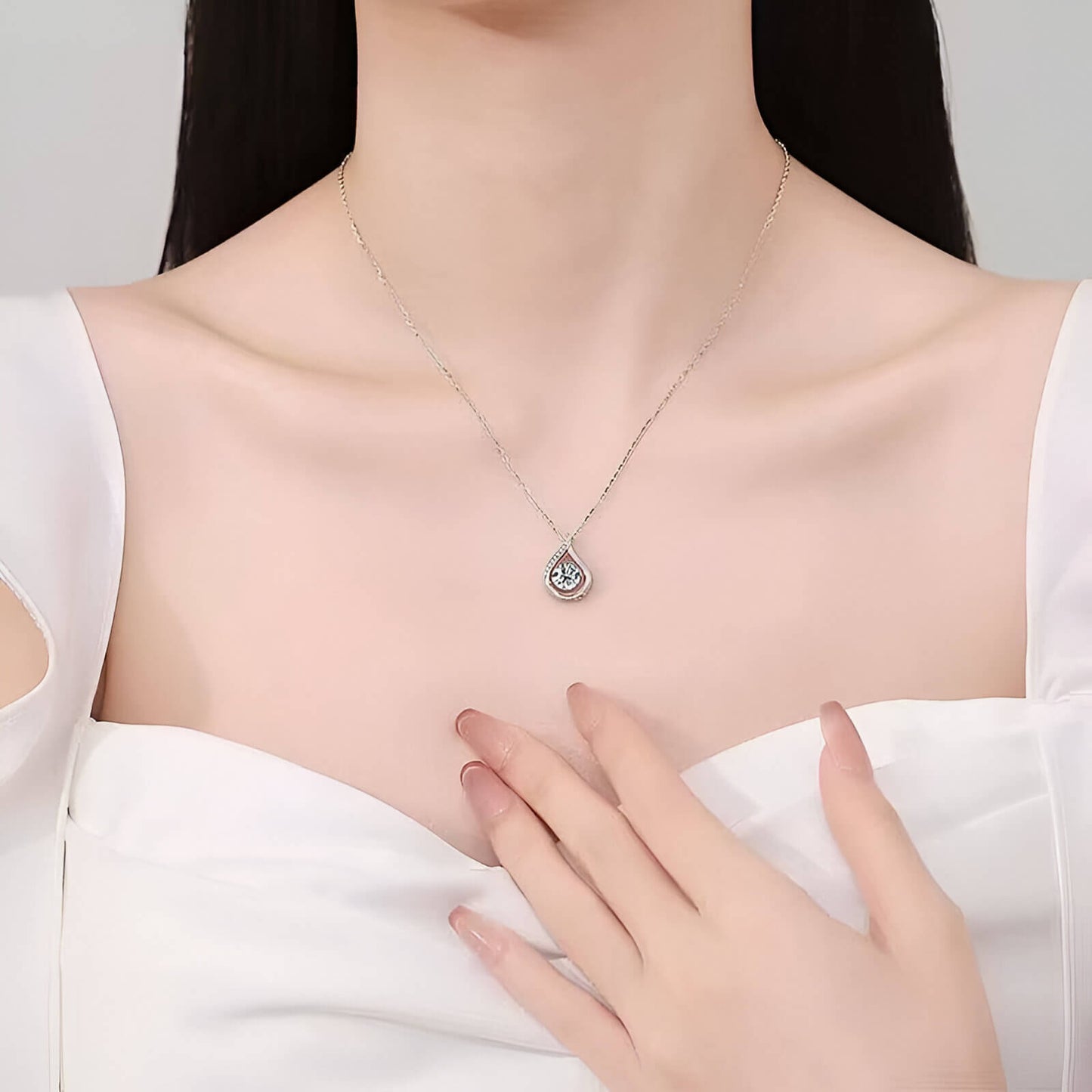 Collier goutte serti tension en or blanc orné de diamants naturels & synthétiques porté au cou d'une femme vue de loin.