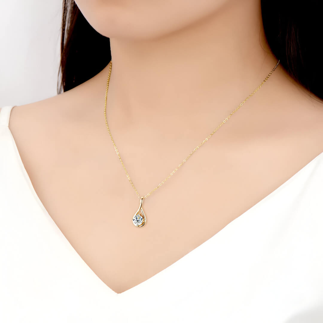 Pendentif goutte solitaire en or jaune et diamant synthétique porté au cou d'une femme.
