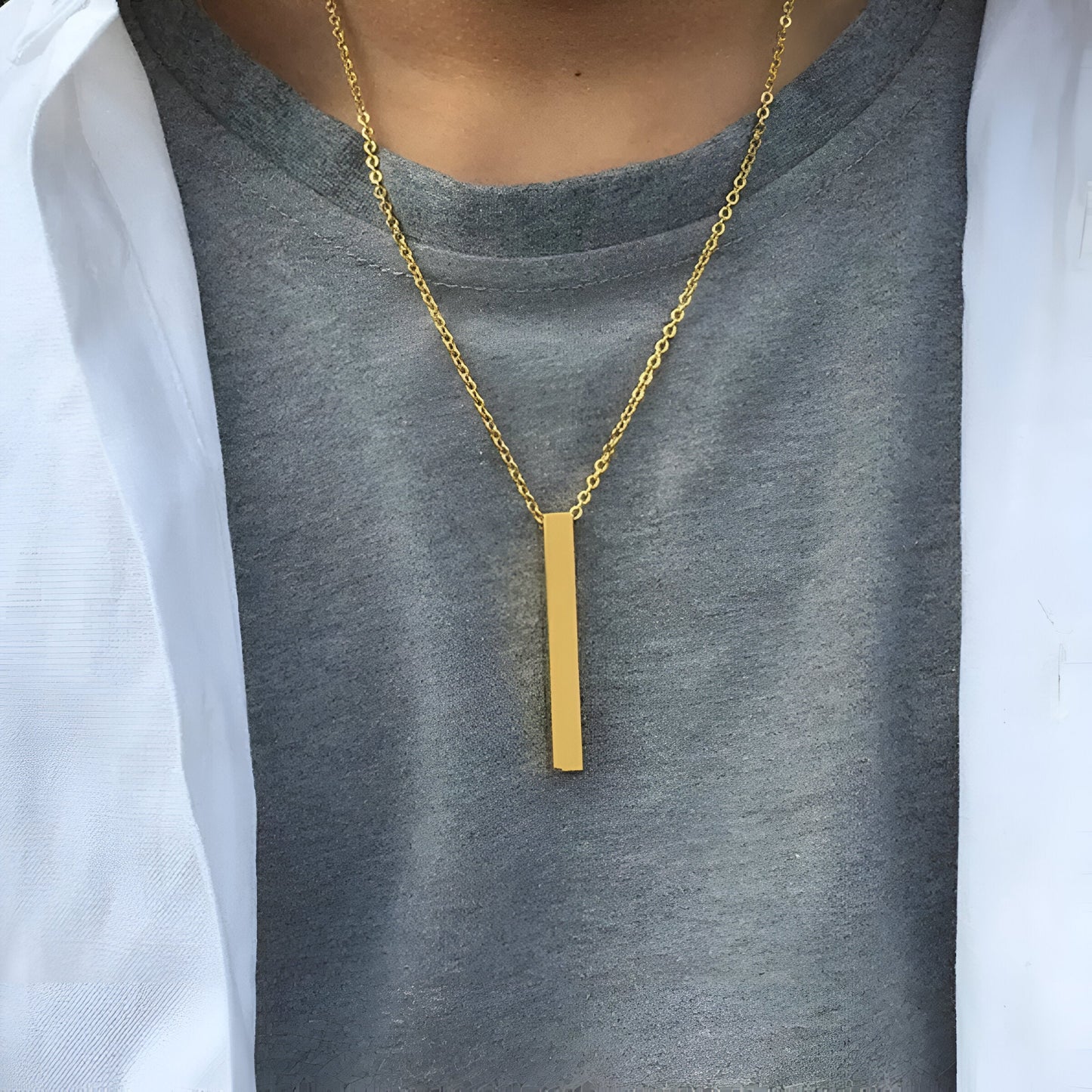 Pendentif rectangulaire fin en or jaune porté au cou d'un homme.