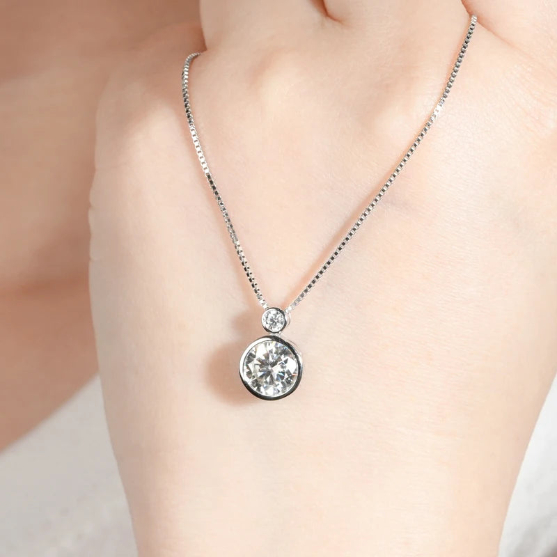 Pendentif serti clos en or blanc et diamants synthétiques sur une main de femme.