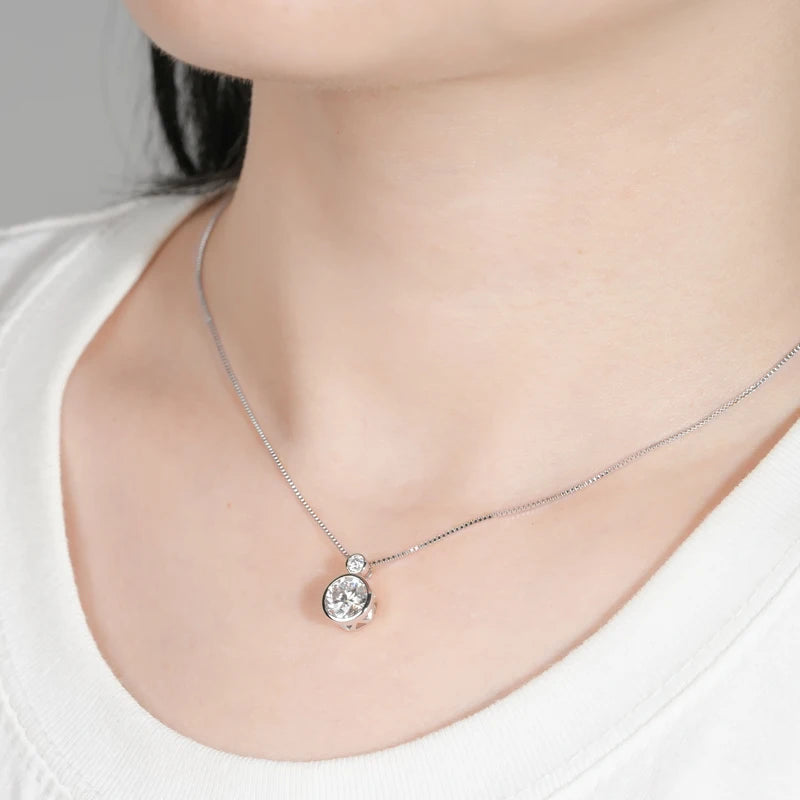 Pendentif serti clos en or blanc et diamants synthétiques porté au cou d'une femme.