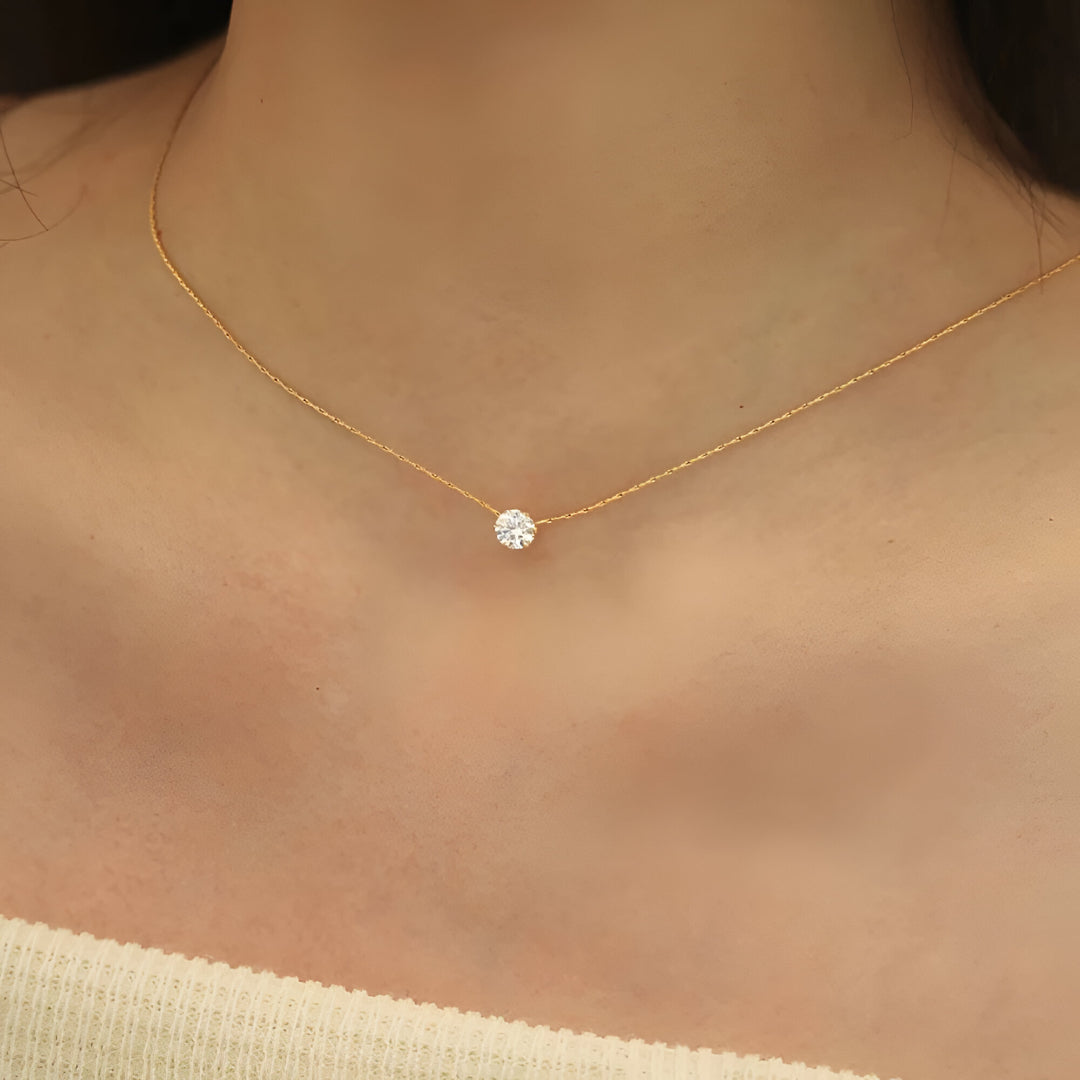 Pendentif solitaire en acier doré et diamant naturel porté au cou d'une femme.