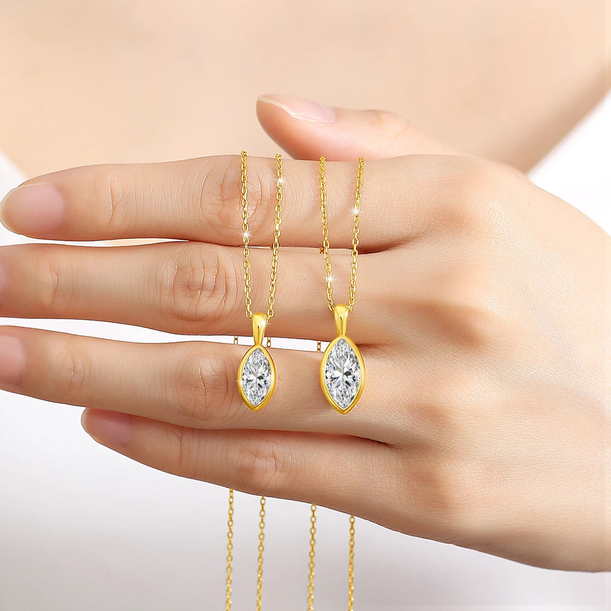 Pendentif solitaire navette en or jaune et diamant synthétique 1 carat et 2 carats sur une main de femme.