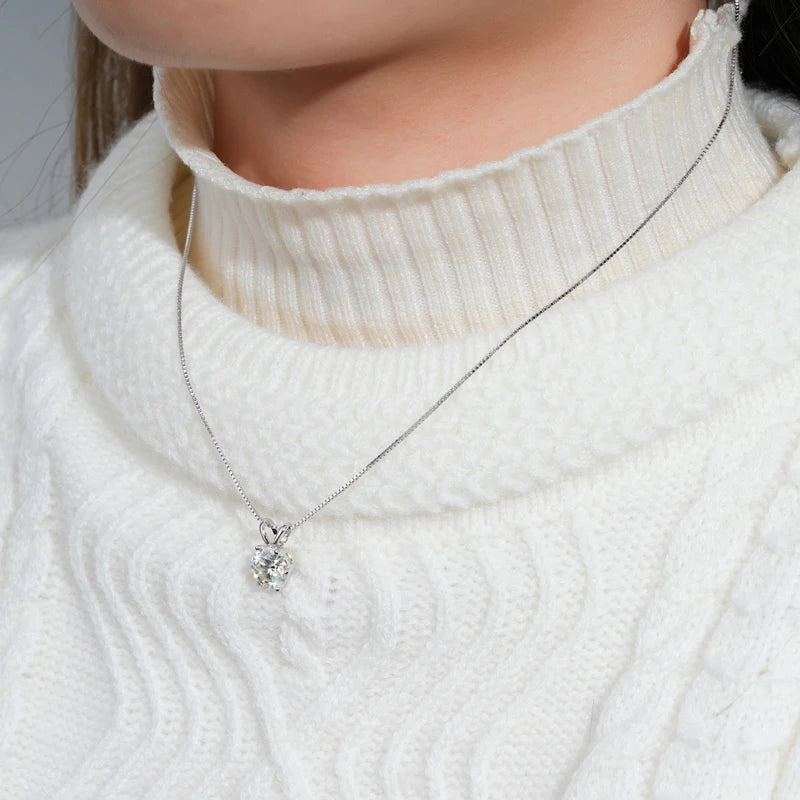 Collier endentif solitaire en or blanc et diamant synthétique porté au cou d'une femme vue de face.