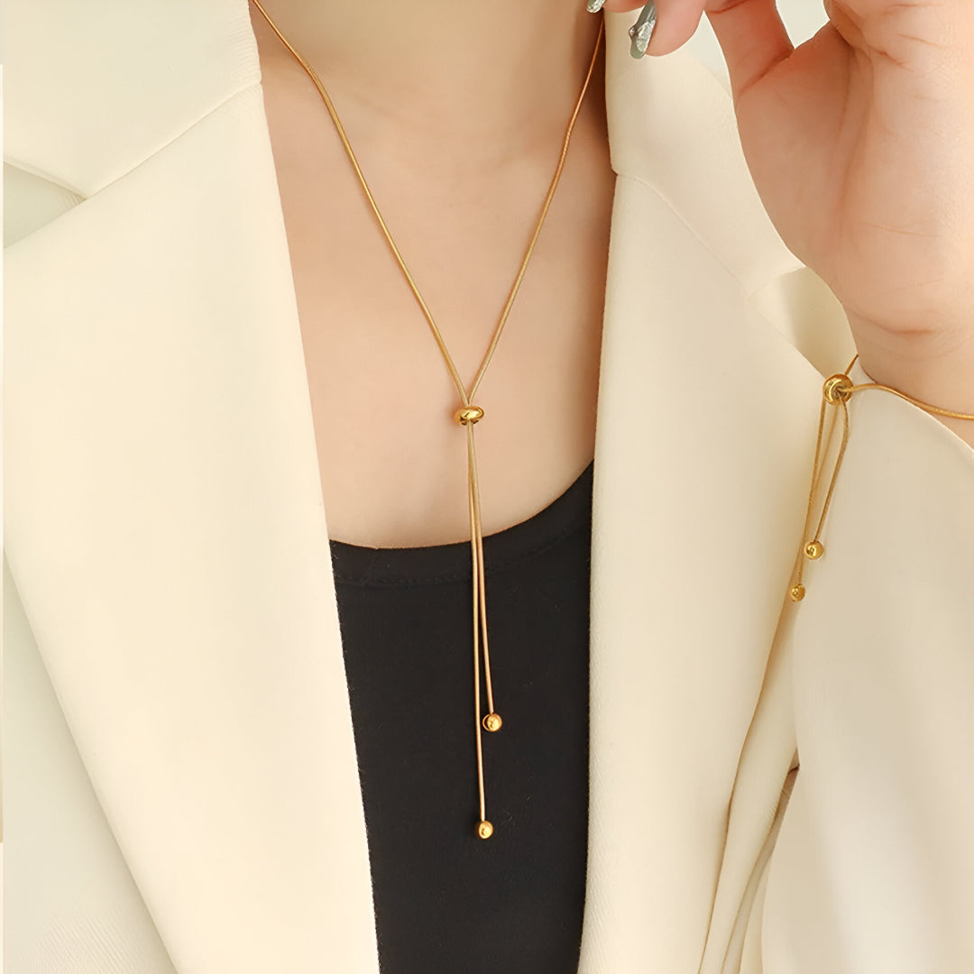 Sautoir perle synthetique amovible en acier doré orné d'une perle amovible porté au cou d'une femme.