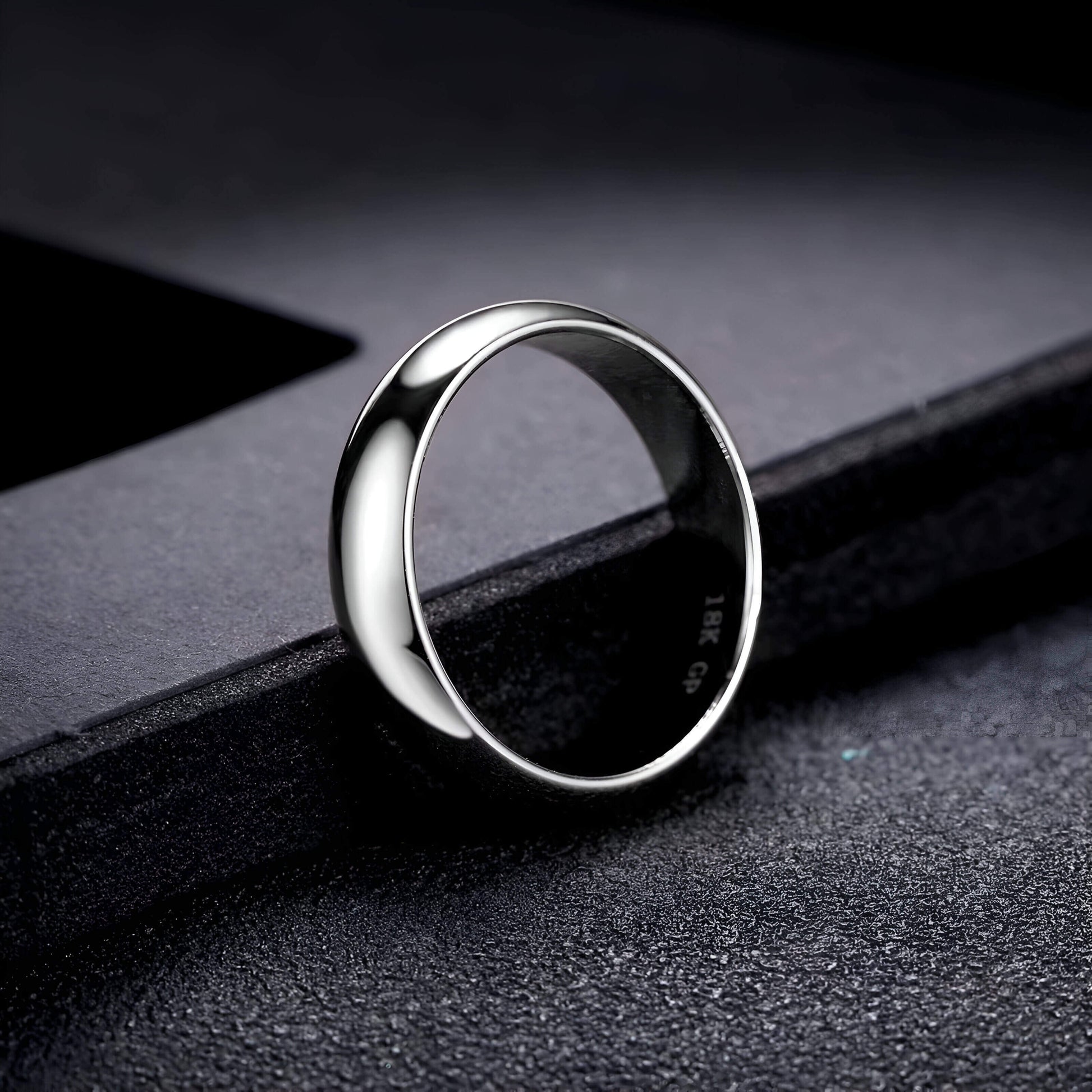 Alliance classique de mariage en acier inoxydable posée sur un rebord noir.