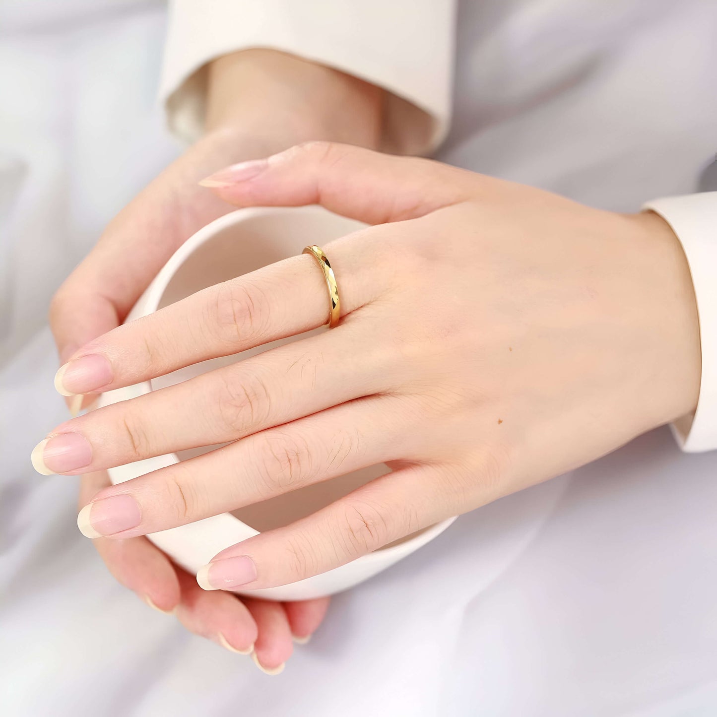 Alliance facettée de 4mm en tungstène et or jaune portée au doigt d'une femme vue de loin.