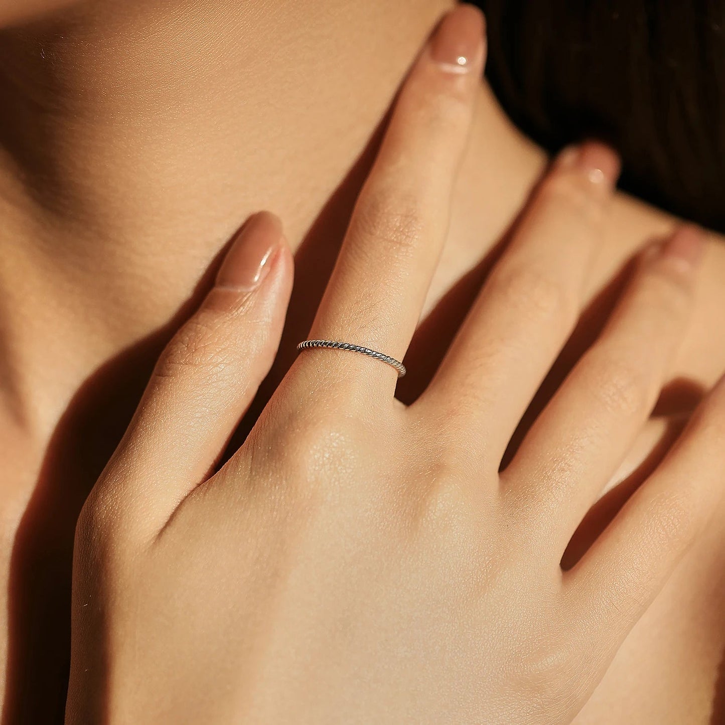 Alliance fine twistée Evelisya en argent 925 plaqué or blanc portée au doigt d'une femme vue de face.