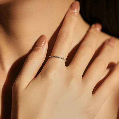 Alliance fine twistée Evelisya en argent 925 plaqué or blanc portée au doigt d'une femme vue de face.