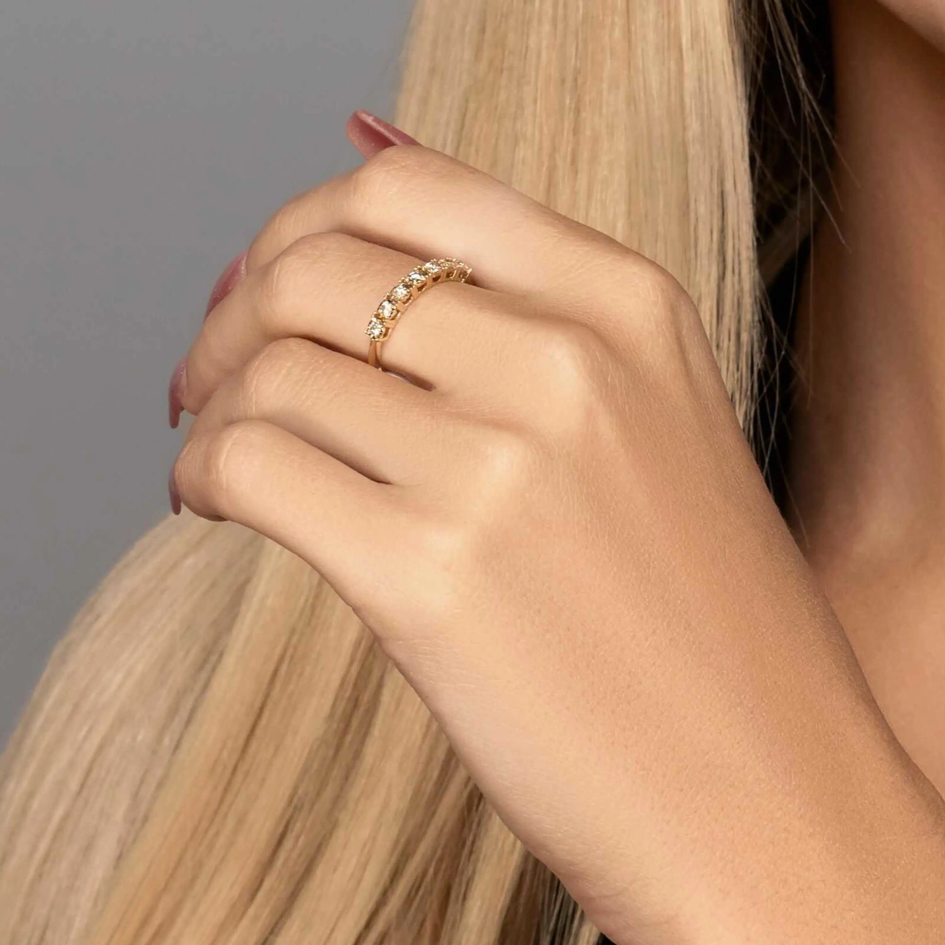 Alliance semi-éternité en or jaune et diamants synthétiques portée au doigt d'une femme.