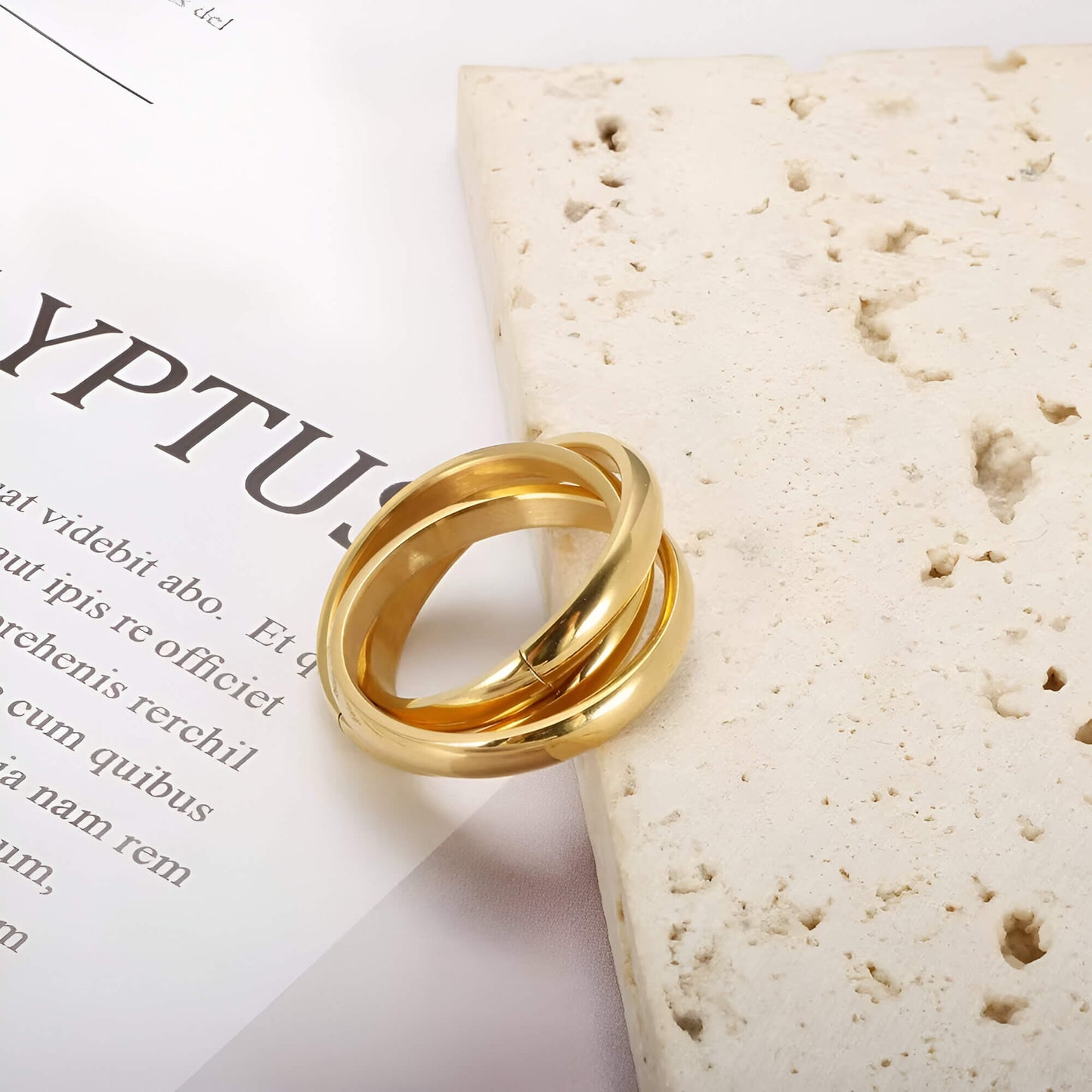 Alliance triple demi-jonc en acier plaqué or jaune posée sur une pierre blanche.